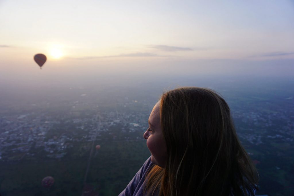 Zoe looking out from the hot air balloon, out of focus in the background is another balloon and the sun